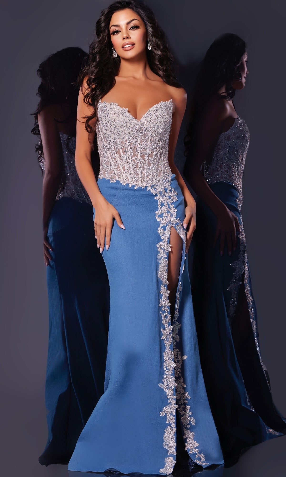 A woman wearing the Jovani 43341 long prom dress, featuring a strapless denim design with a lace embellished corset bodice and blue skirt with a high leg slit and floral lace trim, stands in front of a mirror.